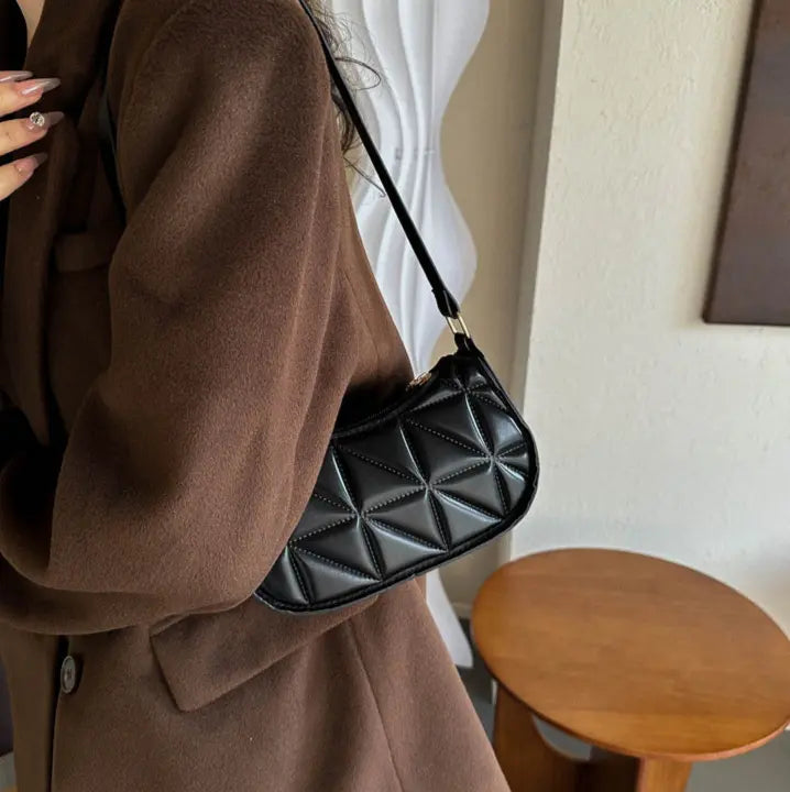 Sac bandoulière noir porté à l’épaule avec bandoulière ajustée.