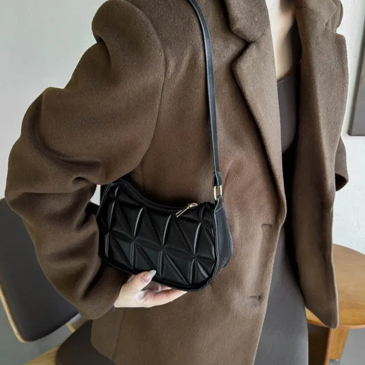 Sac bandoulière noir porté à l’épaule avec bandoulière ajustée.