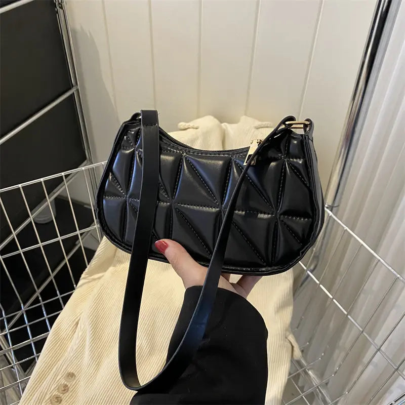 Sac bandoulière noir porté à l’épaule avec bandoulière ajustée.