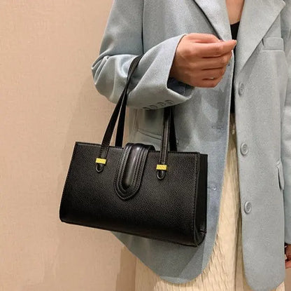 Sac cuir végan noir porté à l’épaule avec bandoulière ajustable.
