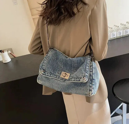 Sac denim bleu délavé porté à l’épaule avec bandoulière simple.