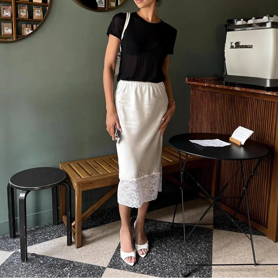 Jupe midi satinée noire avec finition en dentelle, portée avec un blazer blanc et des escarpins 